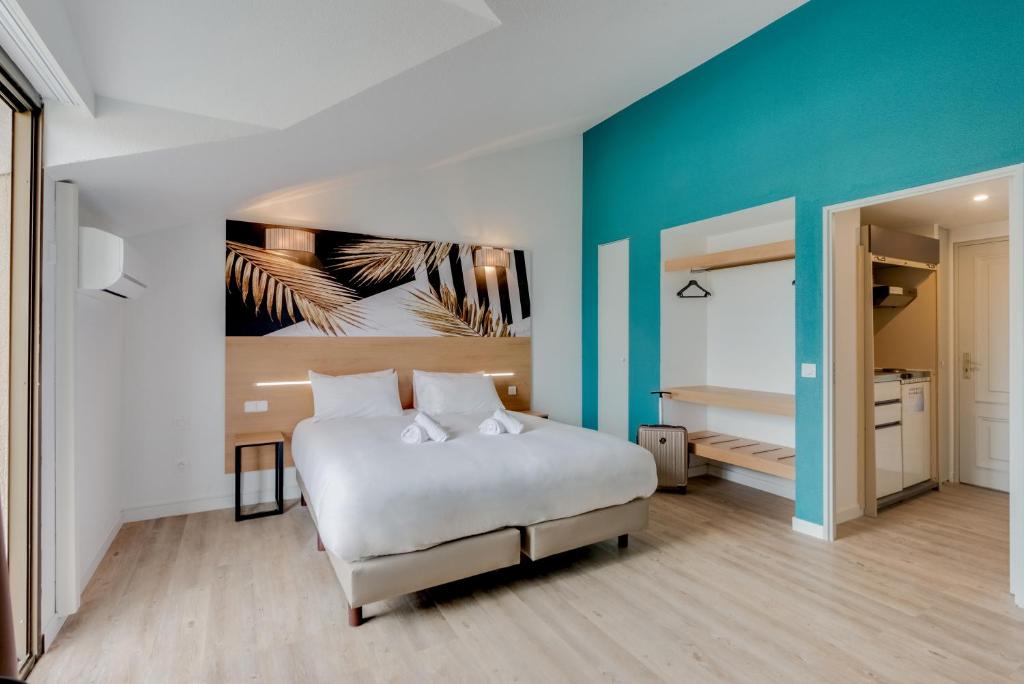 カンヌにあるレジドホテル レ コラリヌのベッドルーム1室(白いベッド1台、青い壁付)