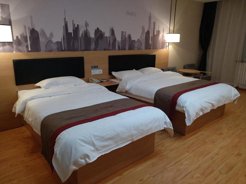two beds in a hotel room with a city painting on the wall at Thank Inn Chain Hotel Qinghai Yushu County Kangba Commercial City in Yushu