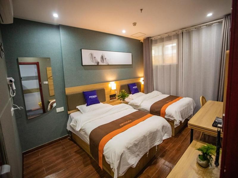 a hotel room with two beds and a mirror at JUN Hotels Jiangsu Nanjing Hongyuan Avenue Subway Station in Nanjing