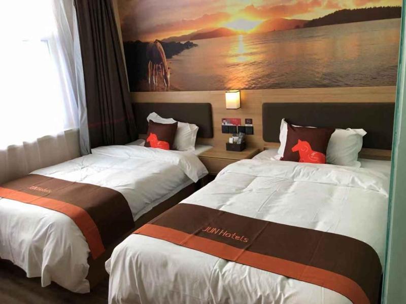 two beds in a hotel room with a painting on the wall at JUN Hotels Shandong Liaocheng Dong'a County Bus Station Store in Liaocheng