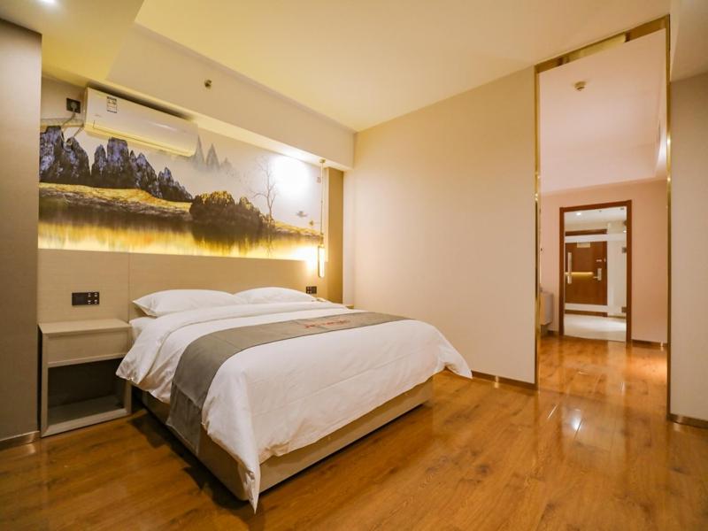 a bedroom with a large bed and a painting on the wall at JUN Hotels Liaoning Anshan Railway Station Wanxianghui in Anshan
