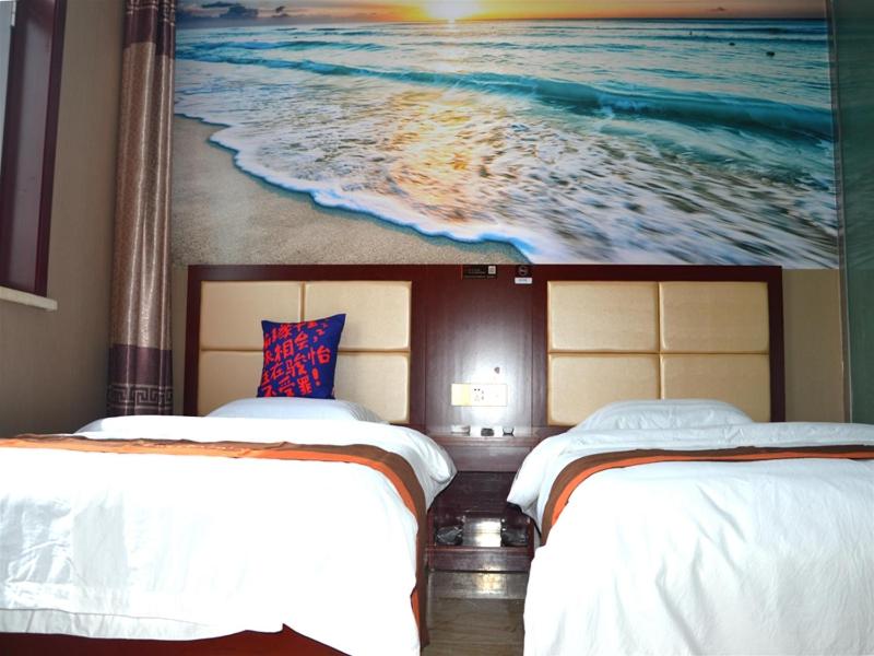 a bedroom with two beds and a painting of the ocean at JUN Hotels Shanxi Lvliang Lishi District Lvliang Academy West Gate in Luliang