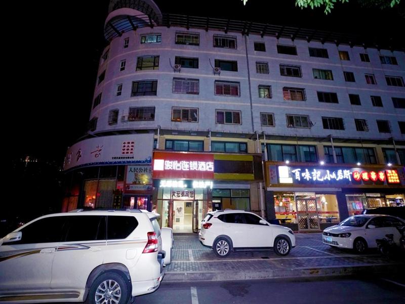 dos autos estacionados en un estacionamiento frente a un edificio en JUN Hotels Gansu Jiayuguan Jingtie District Guanghui Community, en Jiayuguan