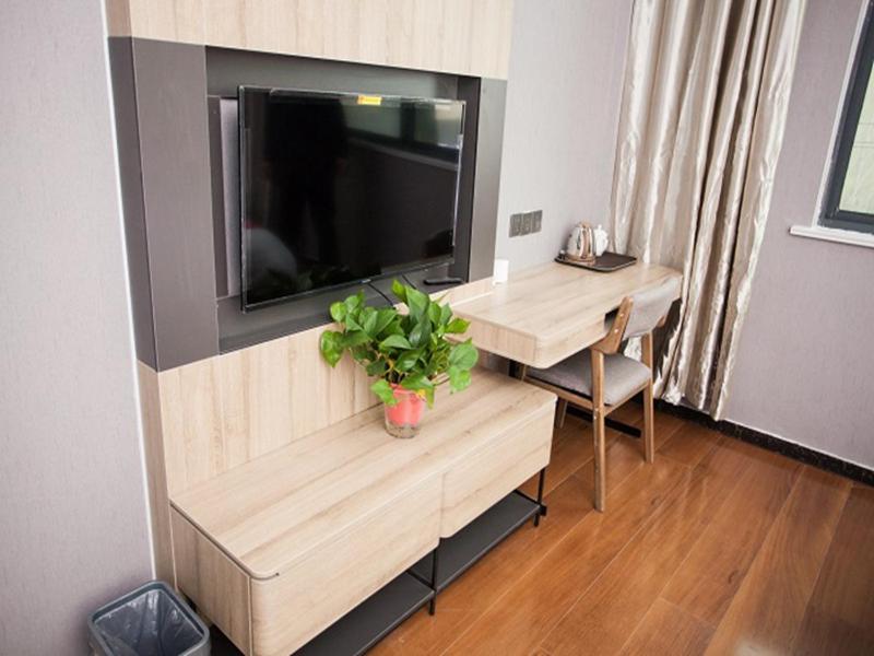a living room with a tv and a desk with a plant at JUN Hotels Shandong Heze Development Zone Shanghai Road in Xinji