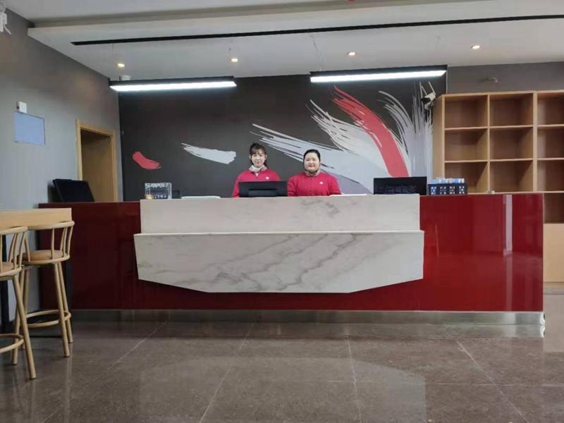 two people standing at a counter in a lobby at Thank Inn Chain Hotel Luoyang Mengjin County Yellow River Avenue Bus Station in Luoyang