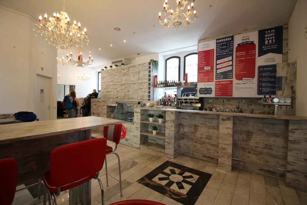 un restaurante con un bar con sillas rojas y lámparas de araña en New Generation Hostel Milan Center Navigli en Milán