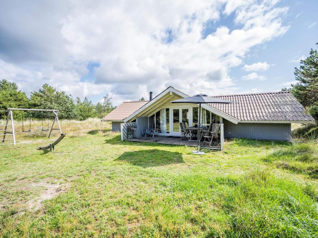 una pequeña casa en un campo con un columpio en Holiday home Blåvand CXLVI, en Blåvand