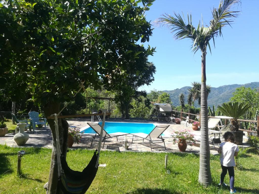 a boy standing in a yard with a hammock next to a pool at Le Muse Country House - Gole Alcantara in Motta Camastra