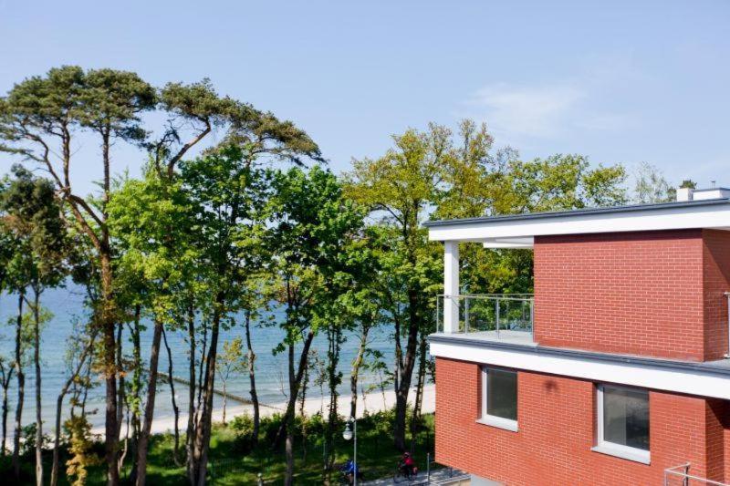 a red building with trees in front of a beach at Resort Apartamenty Klifowa Rewal 31 in Rewal