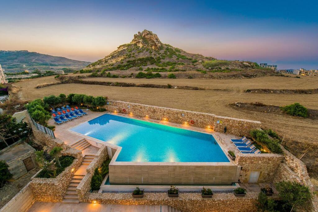 an outdoor swimming pool with chairs and a mountain at A Bed Of Roses in Marsalforn