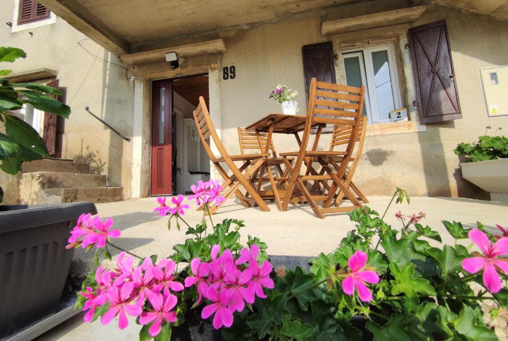 2 chaises et une table sur une terrasse couverte avec des fleurs roses dans l'établissement Apartman Josip, à Garica