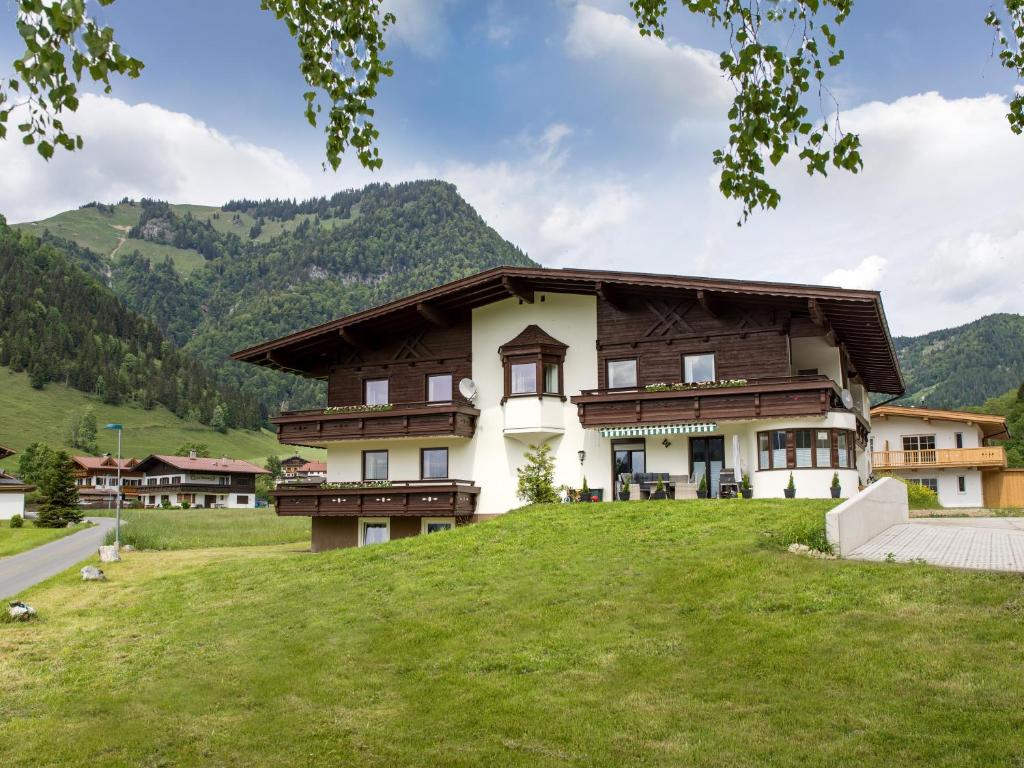 a large house on a grassy hill with mountains in the background at Appartementhaus Montana KG in Walchsee