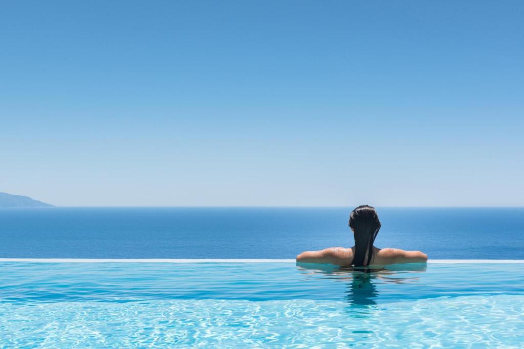 une femme assise dans l'eau de l'océan dans l'établissement Blue Horizon Villas with Private Pool & Sea View, à Plateies