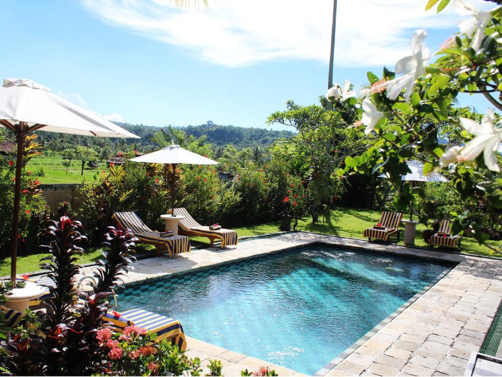 a swimming pool with chairs and umbrellas in a yard at Puri Bagus Manggis in Candidasa