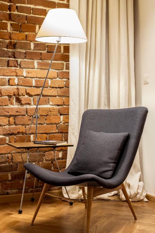 Gray upholstered lounge chair beside lit floor lamp, small side table, exposed brick wall, warm ambience.