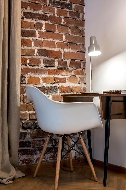 White molded chair at wooden desk beneath lit desk lamp against exposed brick wall.
