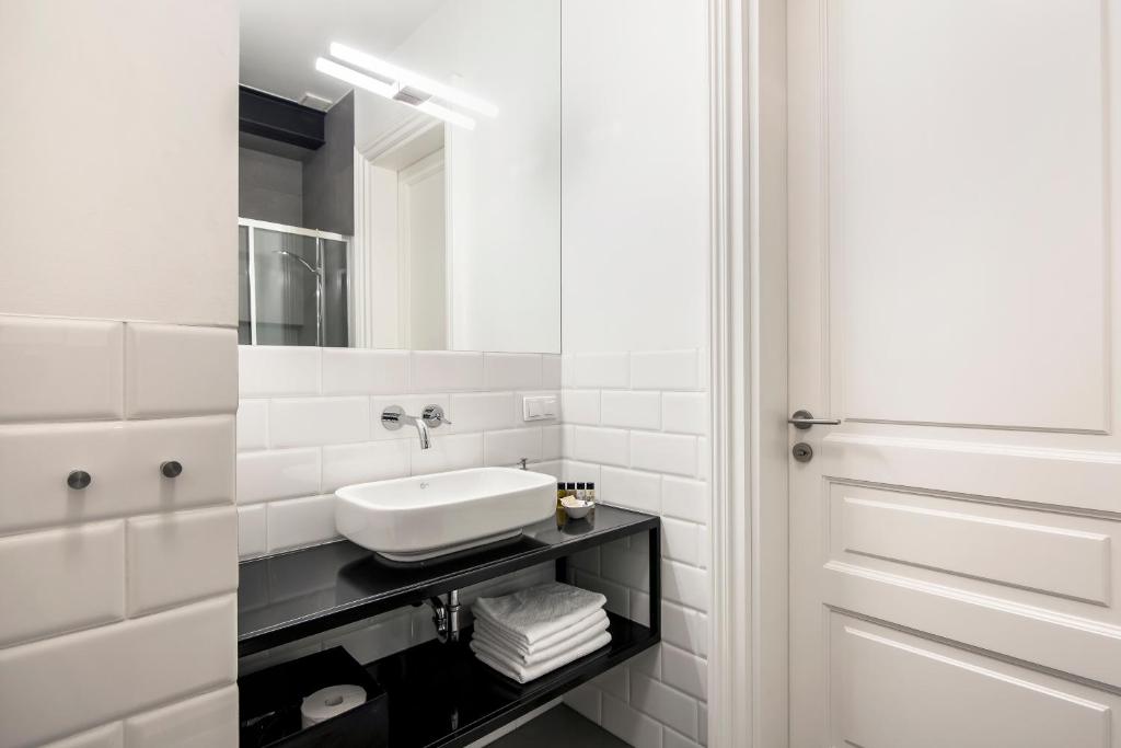 Sleek bathroom sink and wall-mounted faucet above black shelf holding folded towels and toiletries.