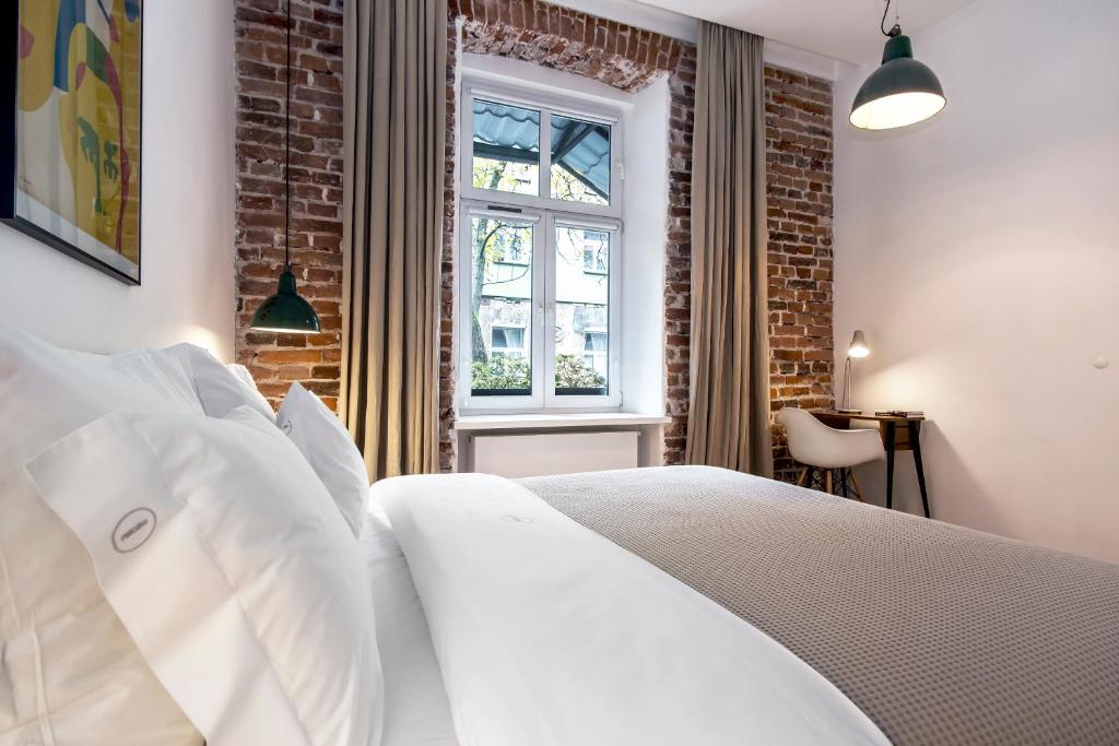 Crisp white pillows and gray bedspread by window with curtains, brick accents, small desk.