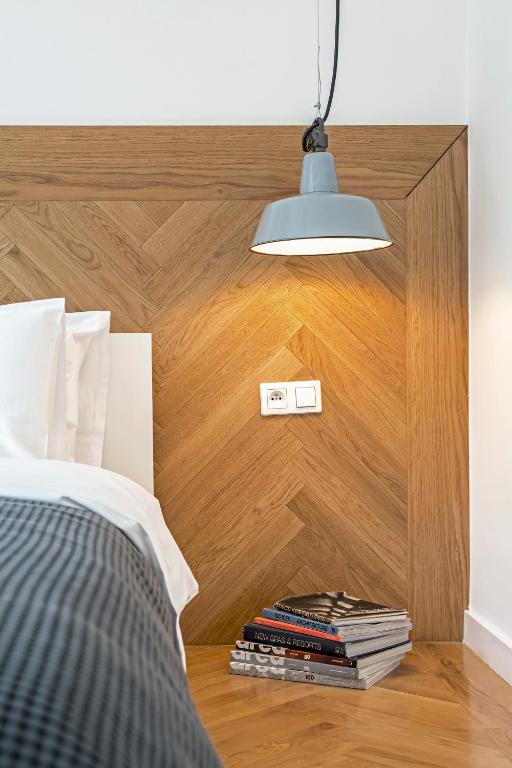 Corner bedside detail: chevron wood panel headboard, lit gray pendant lamp, stack of magazines.
