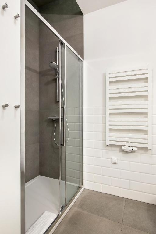 Glass shower enclosure with handheld showerhead, gray tile interior, white heated towel radiator nearby.