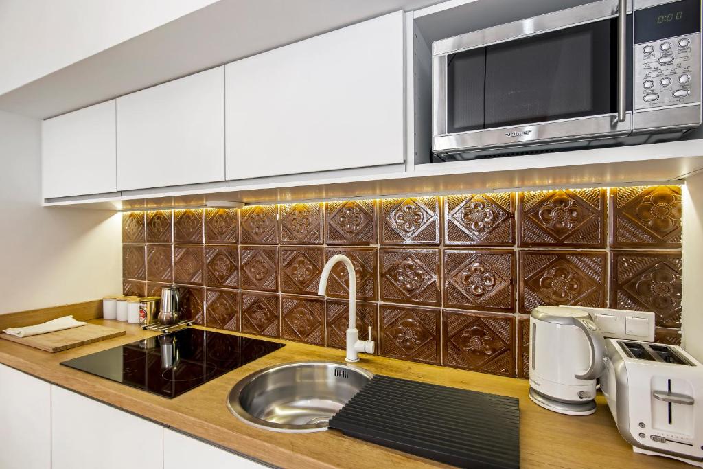 Kitchen countertop close-up with sink, induction hob, toaster, kettle, patterned brown tile backsplash.