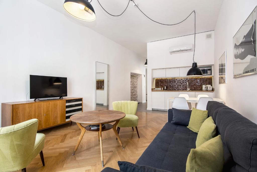 Living room angle with round wooden coffee table, TV console, sofa, kitchenette in background.