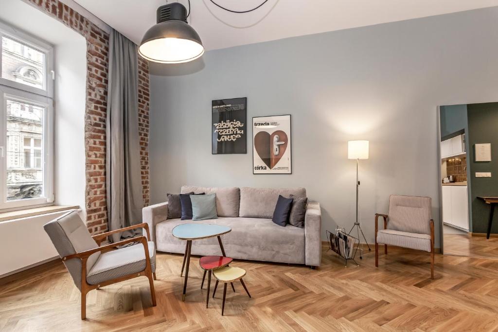 Cozy living room with grey sofa, colorful nesting tables, pendant lamp, exposed brick window, framed art.