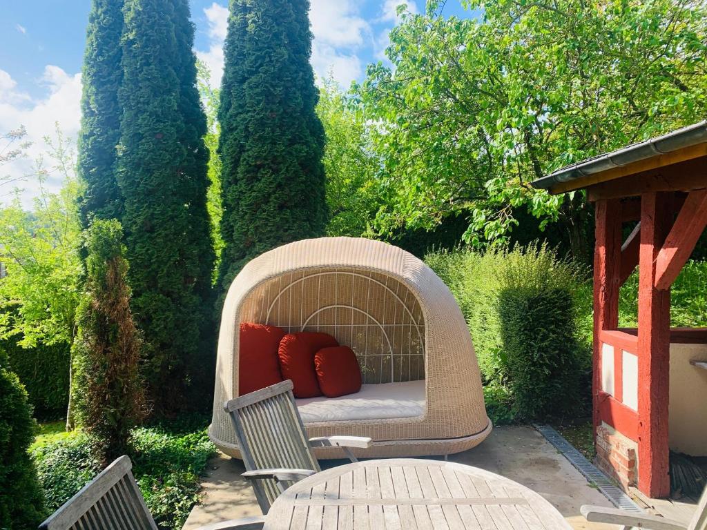 - une chaise en osier avec 2 oreillers rouges sur la terrasse dans l'établissement La Maison Blanche du 10Honfleur, à Honfleur