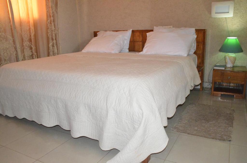 1 dormitorio con 1 cama grande con sábanas y almohadas blancas en Hotel Ambassadors, en Lomé