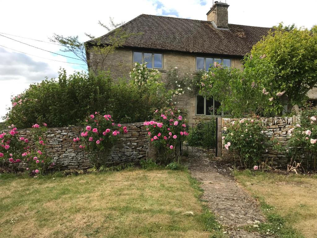 ein Haus mit rosa Blumen und einem Steinzaun in der Unterkunft Rose Cottage, 4 The Hill in Burford