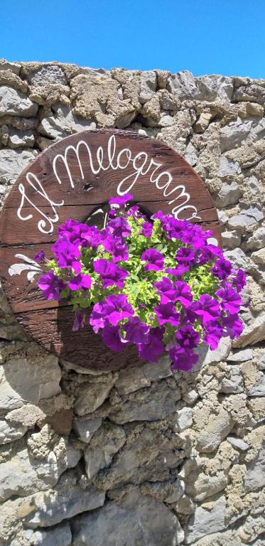 un cartel de bienvenida en una pared de piedra con flores púrpuras en B&B Il Melograno, en Tortorella