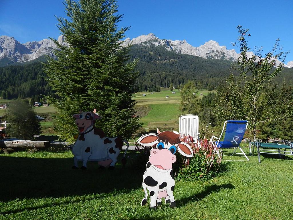 Deux vaches en plastique et une statue de vache dans l'herbe dans l'établissement Residence La Pineta, à Padola