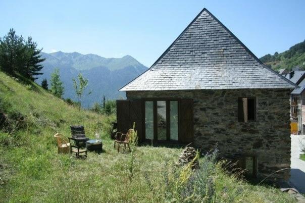 una pequeña casa de piedra en una colina con césped en CABAÑA VENTO NORTE, en Vilamòs