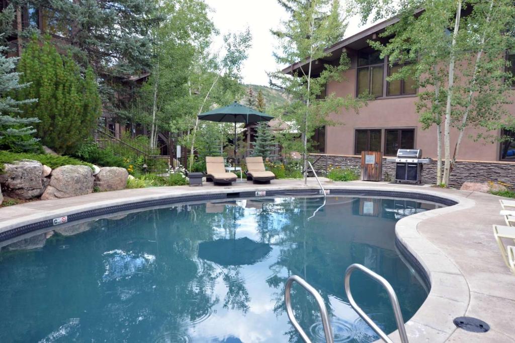 a pool with chairs and an umbrella in a yard at Aspenwood Studio with Loft- J12 in Snowmass Village