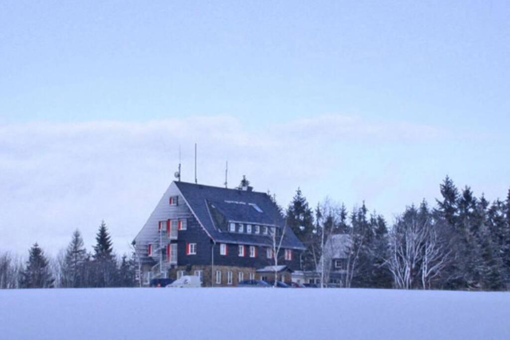 uma casa grande no meio de um campo coberto de neve em Berghaus Falkenhorst em Kurort Altenberg