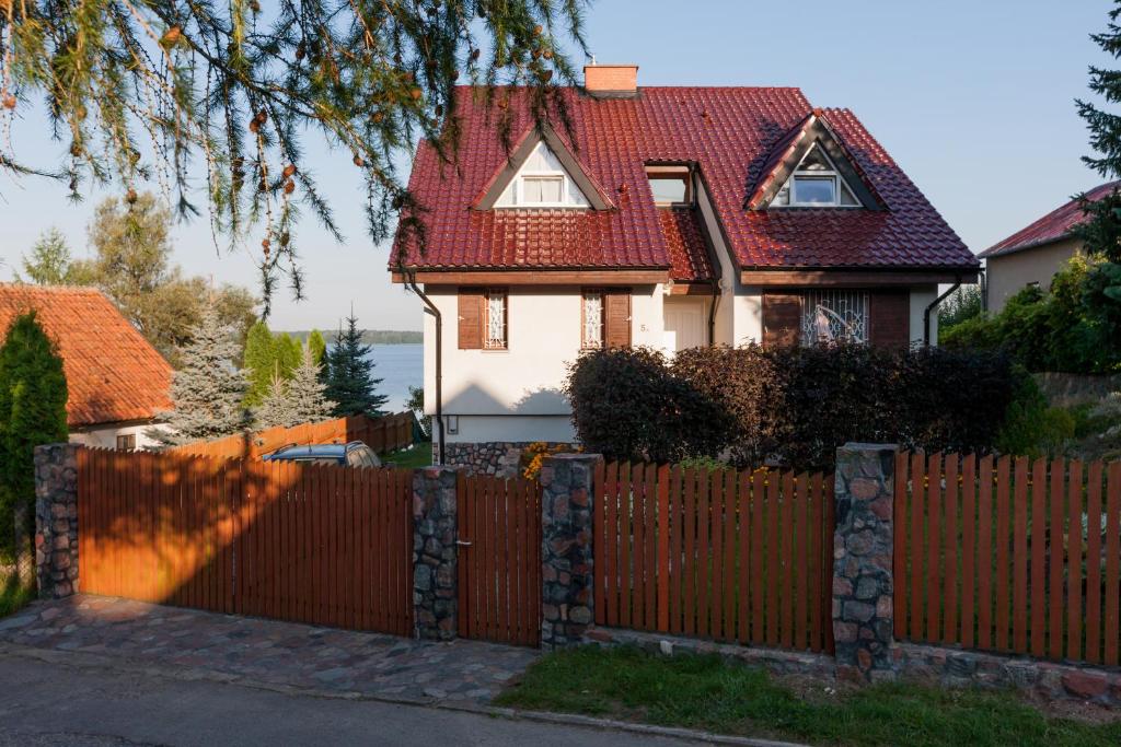 uma casa com uma cerca e um telhado vermelho em Ferienhaus Malgosia direkt am See em Kruklanki