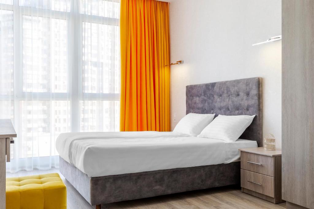 a bedroom with a large bed with an orange curtain at barasport city apartments in Kyiv