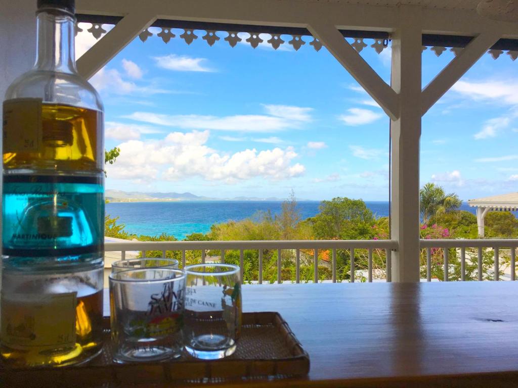 1 Flasche und 2 Gläser auf einem Tisch mit Meerblick in der Unterkunft COEUR SUR LA MAIN in Le Diamant