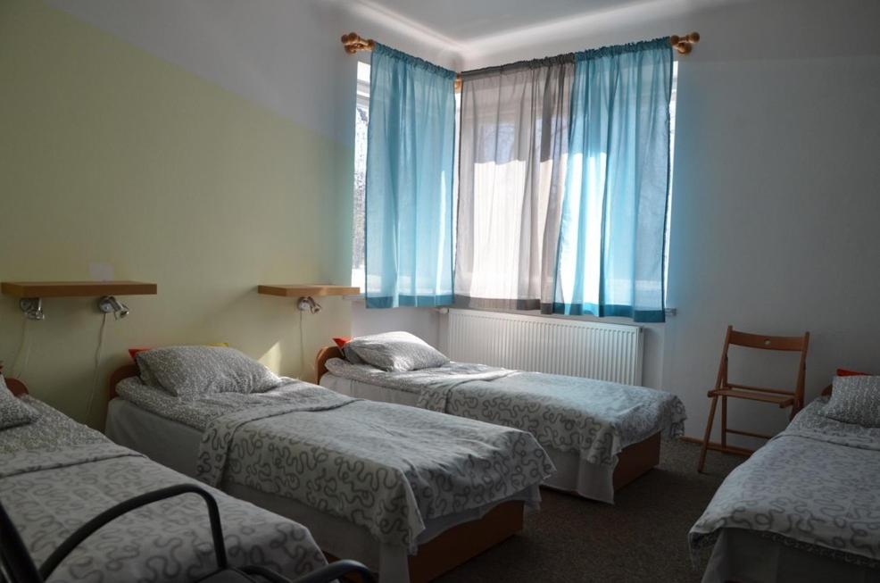 ワルシャワにあるHostel Tolekのベッド3台、青いカーテン付きの窓が備わる客室です。