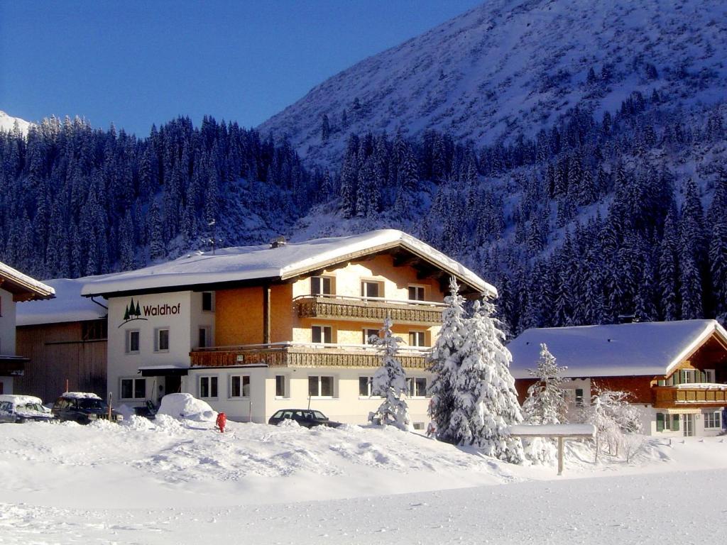 un bâtiment dans la neige devant une montagne dans l'établissement Pension Waldhof, à Lech am Arlberg