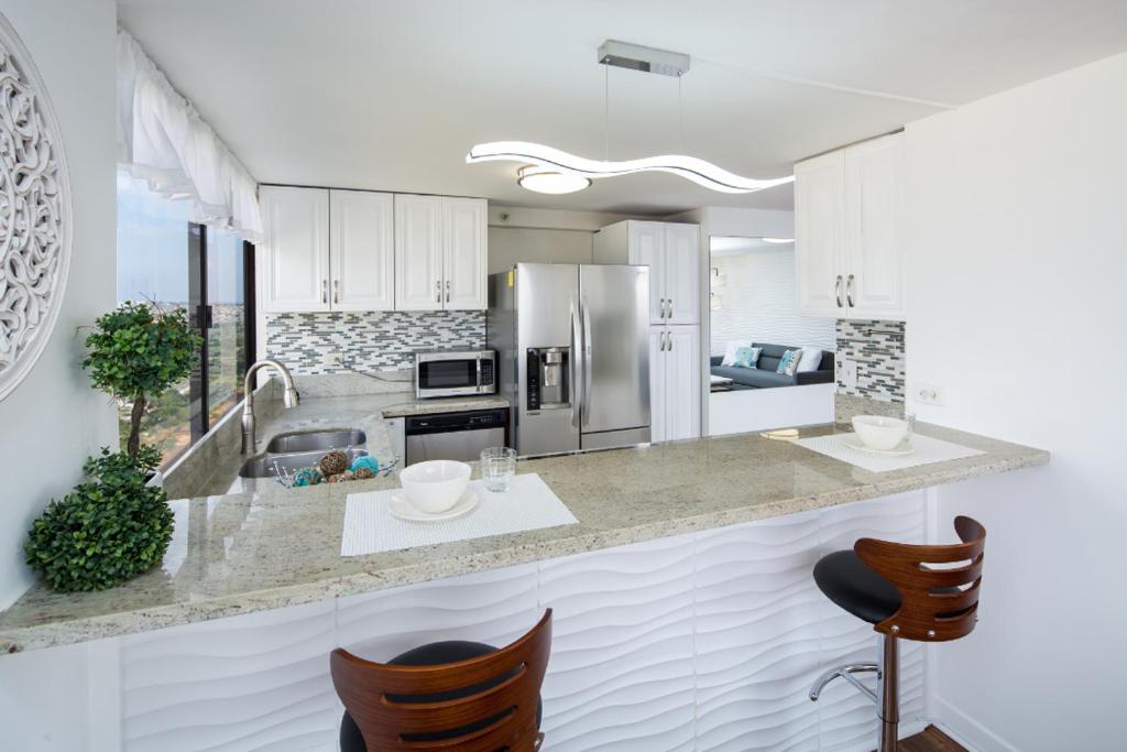 a kitchen with white cabinets and a counter with chairs at Waikiki Penthouse @ The Monarch Hotel in Honolulu