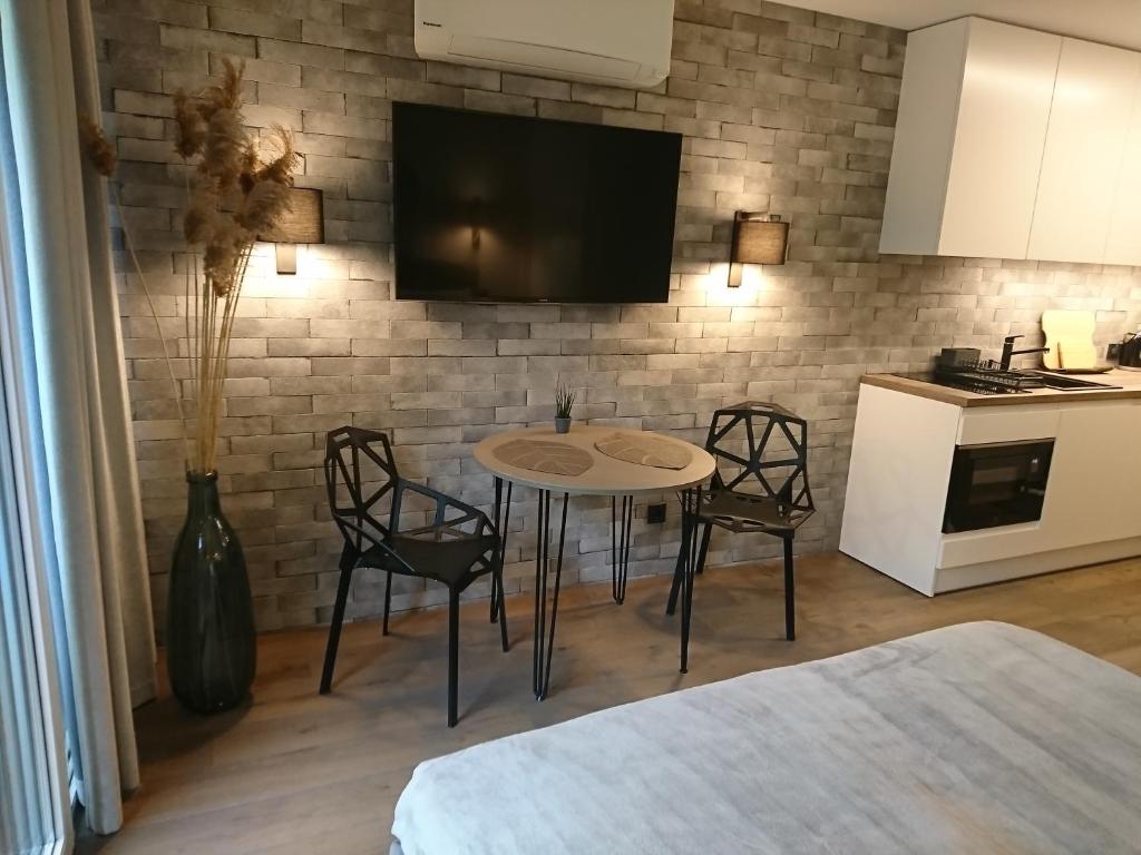 uma cozinha com mesa e cadeiras e uma televisão numa parede de tijolos em Kalno Studijos em Juodkrantė