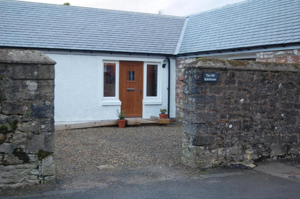 a white house with a brown door and a stone wall at The Old Bakehouse in Newcastleton