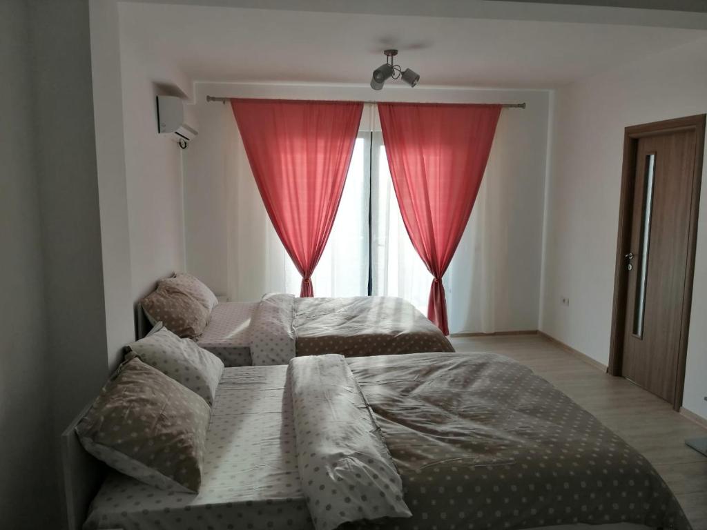 a bedroom with two beds and a window with red curtains at Didy Residence in Eforie Nord