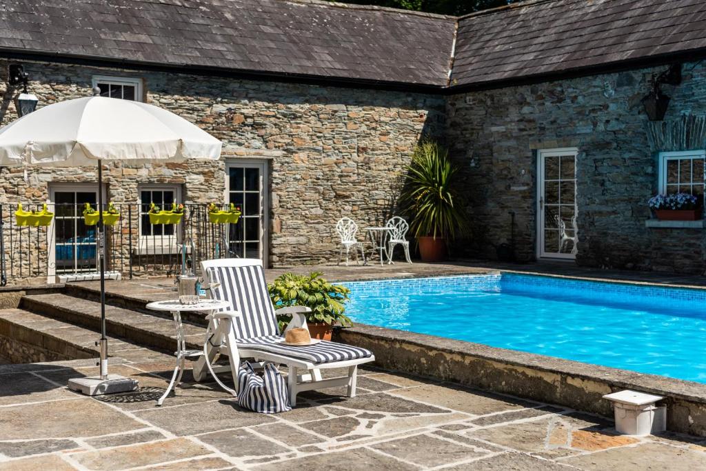 a swimming pool with two chairs and an umbrella at Ardnavaha House - Poolside Cottages in Clonakilty