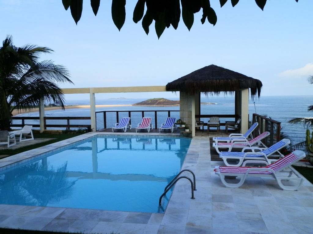 a swimming pool with chairs and a gazebo and the ocean at Setiba Pousada Park in Guarapari