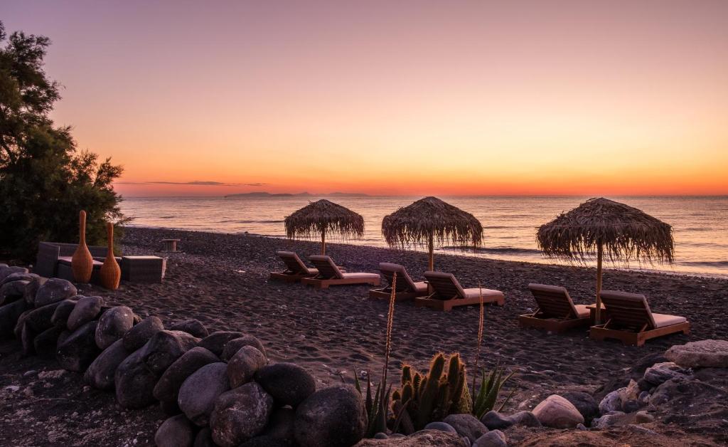 una spiaggia con sedie, ombrelloni di paglia e l'oceano di Beach Houses Santorini a Kamari