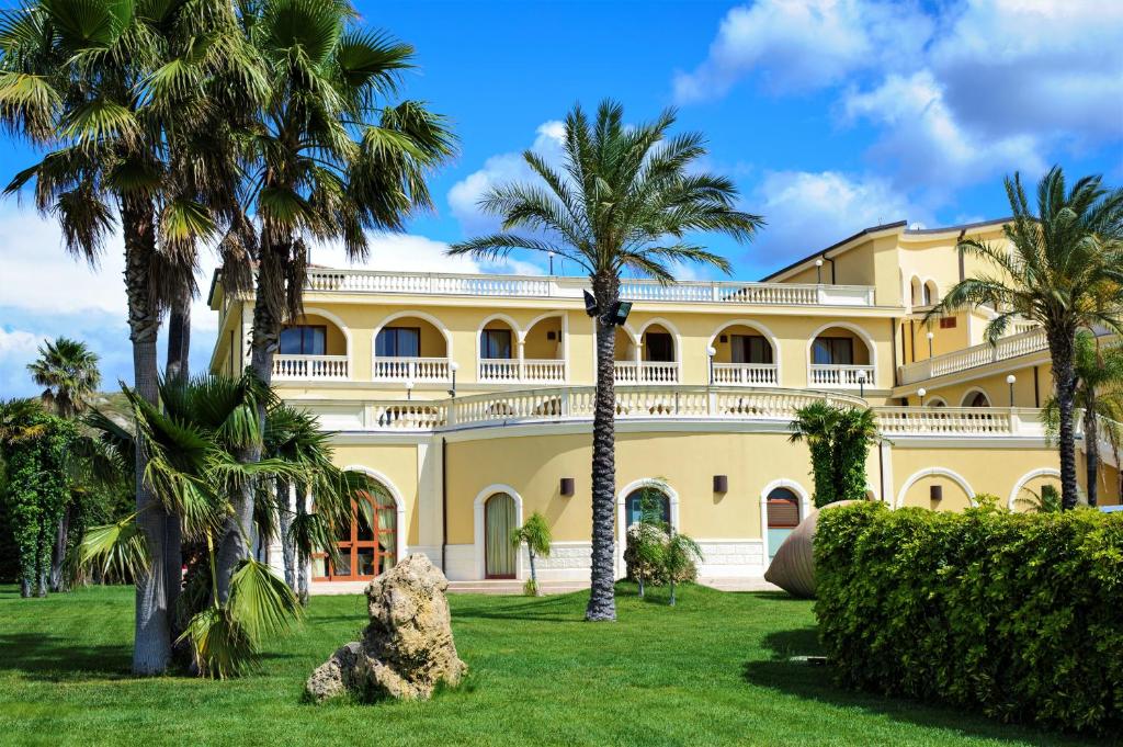 a large yellow building with palm trees in front of it at Parco dei Principi Hotel in Roccella Ionica