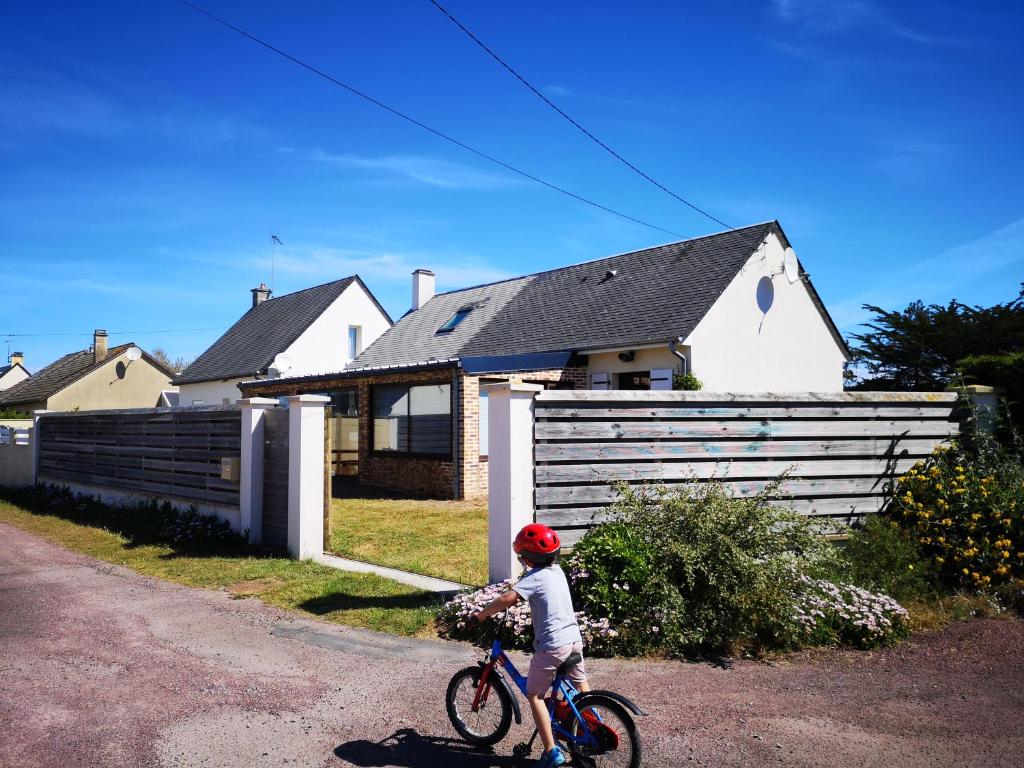uma criança a andar de bicicleta em frente a uma casa em Holiday Home Maison de l'Océan à Denneville em Denneville