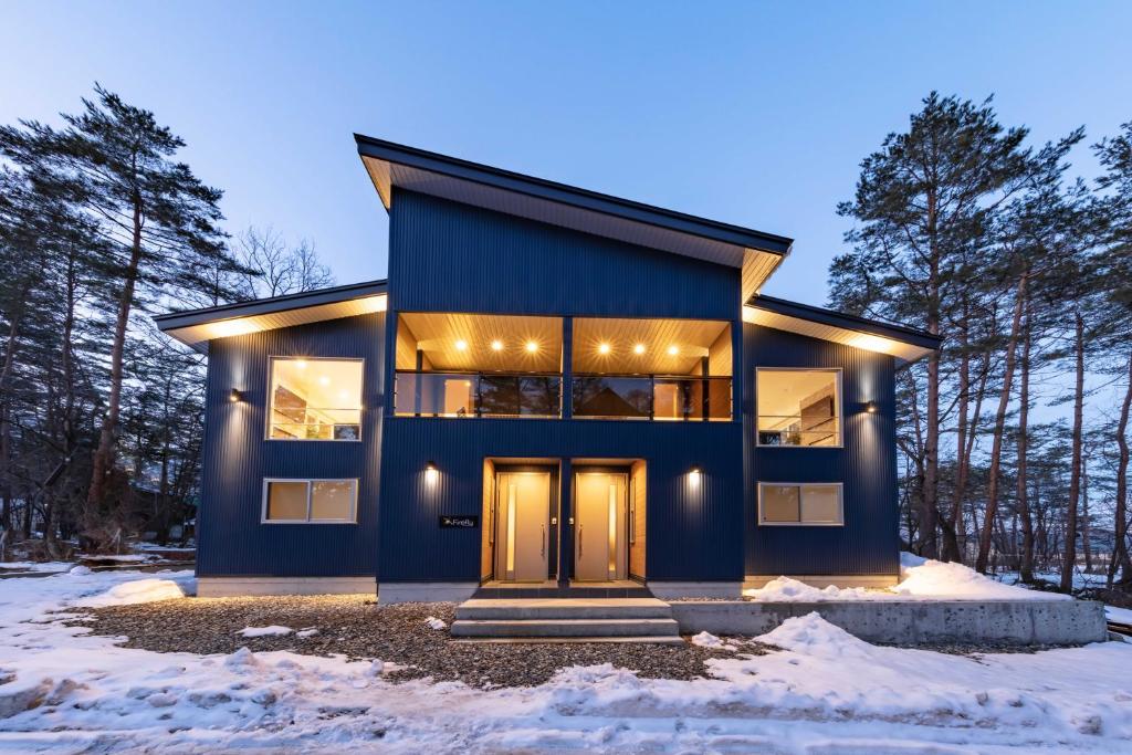 een blauw huis in het bos in de sneeuw bij Firefly Apartments in Hakuba